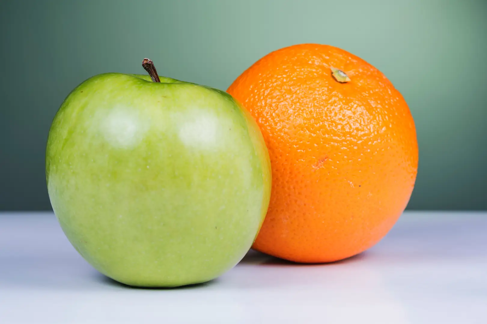 An apple and an orange next to each other on a table.