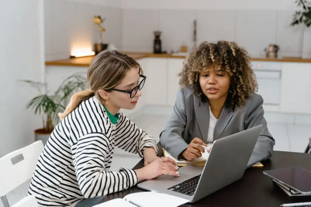 Two people sitting at a table and looking on a macbook together.